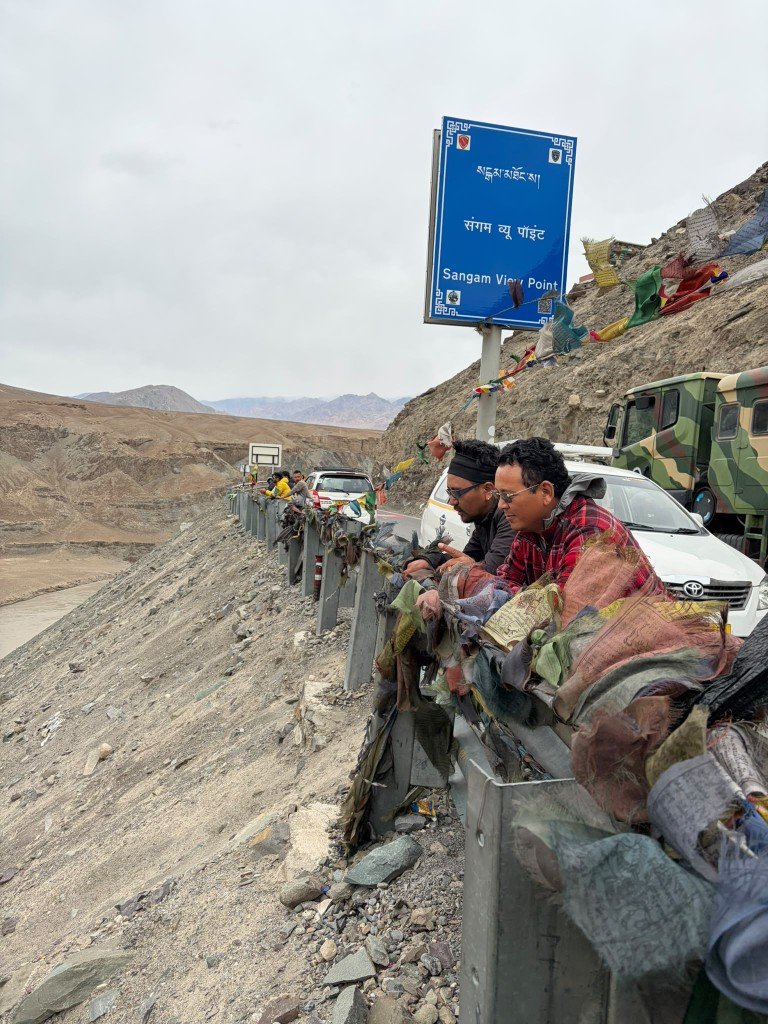 Tashi and Tengeleck at Sangam View Point, beside prayer flags on the guardrail above the river